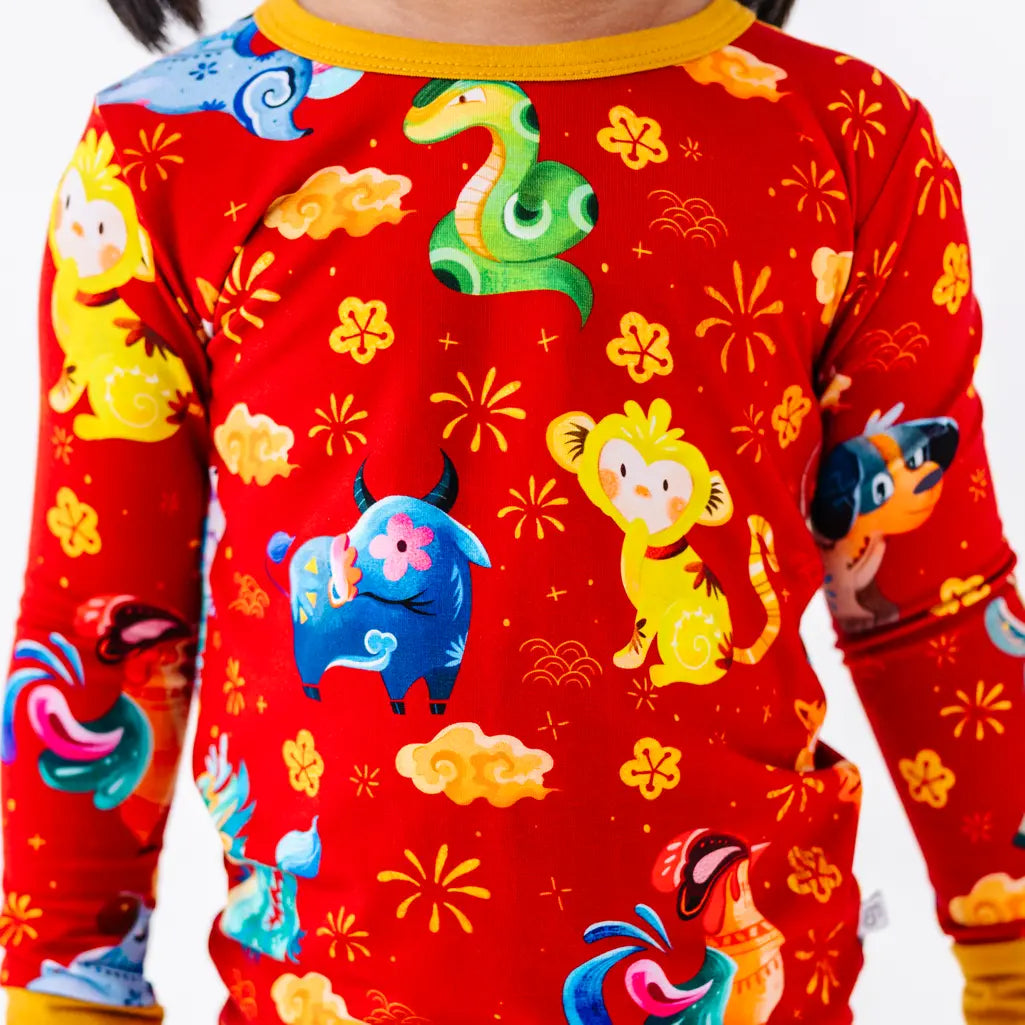 Close up of the front of a long sleeve pajama top with a mustard yellow collar in a red print of zodiac animals and gold clouds.